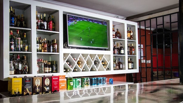 A bar area with shelves of liquor bottles, a television displaying a soccer game, and a bar counter with cans of beer. - Express Inn (Nyeri)