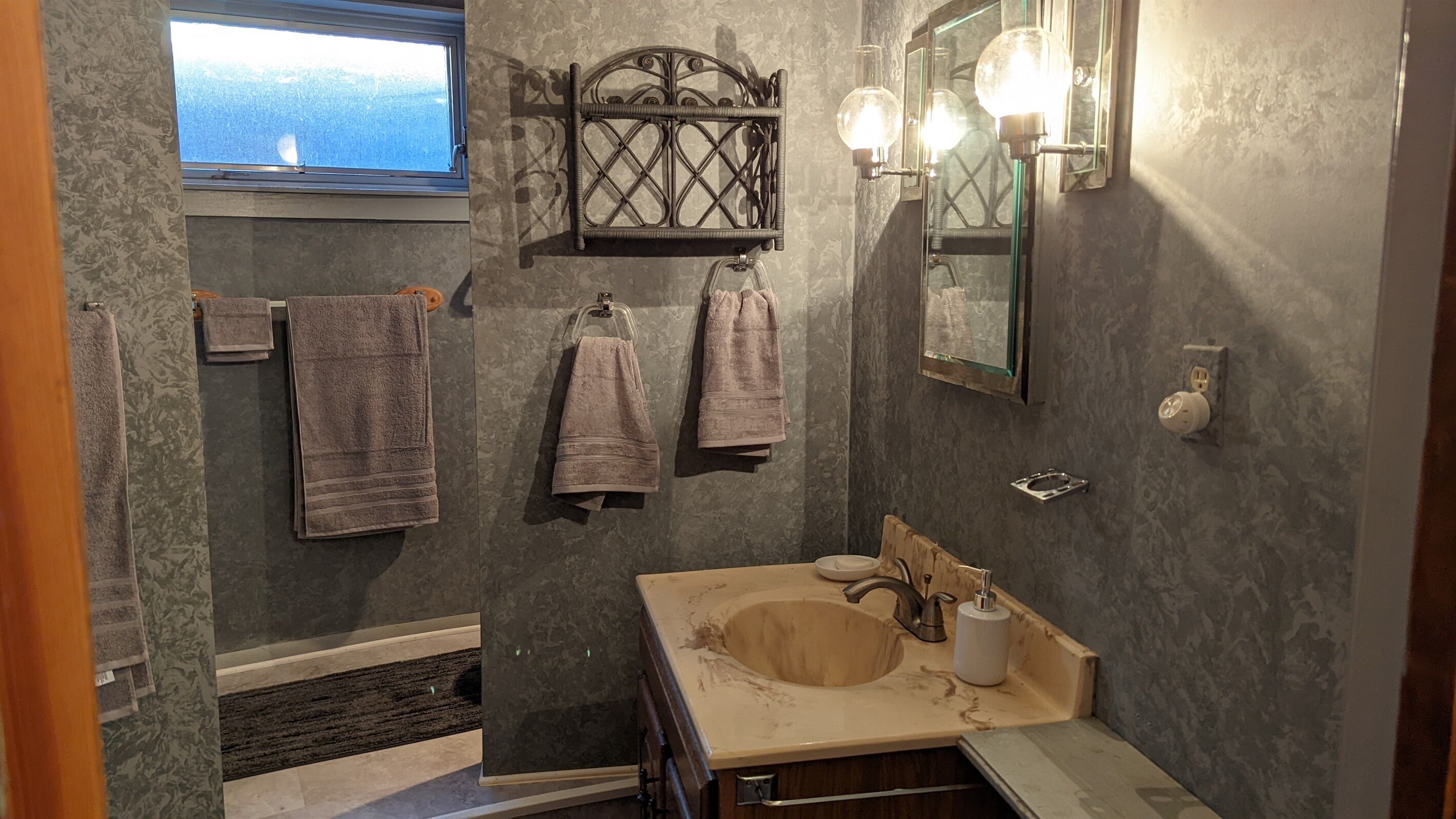 A bathroom with a large window, a sink with a mirror, and towels hanging on a rack.