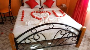 Uma cama bem arrumada com almofadas vermelhas, uma decoração em formato de coração feita de flores vermelhas e uma decoração em forma de cisne na colcha.