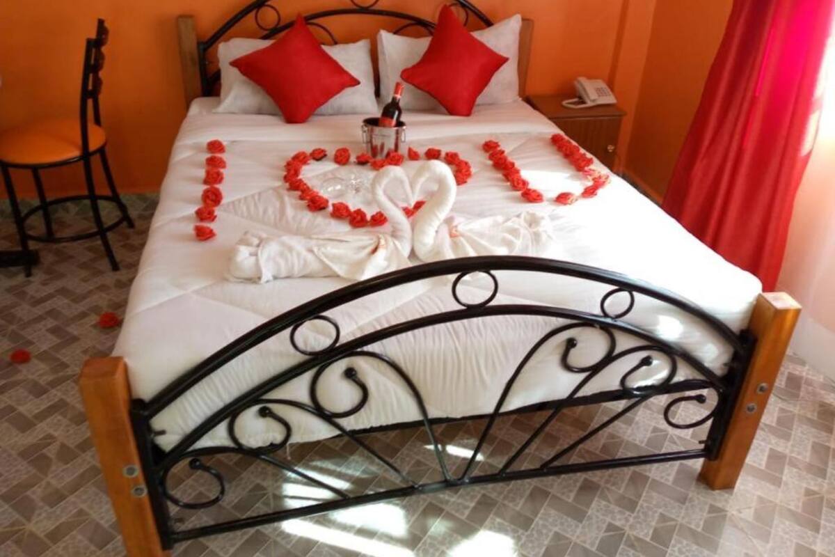 Un lit bien fait, agrémenté d’oreillers rouges, d’une décoration en forme de cœur faite de fleurs rouges et d’une décoration en forme de cygne posée sur le couvre-lit.