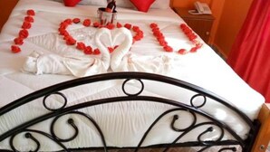 Uma cama com um arranjo de rosas vermelhas em formato de coração e uma garrafa de champanhe.