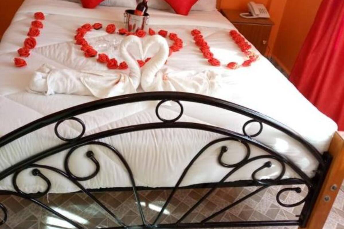 Un lit décoré de roses rouges disposées en forme de cœur, ainsi qu’une bouteille de champagne.