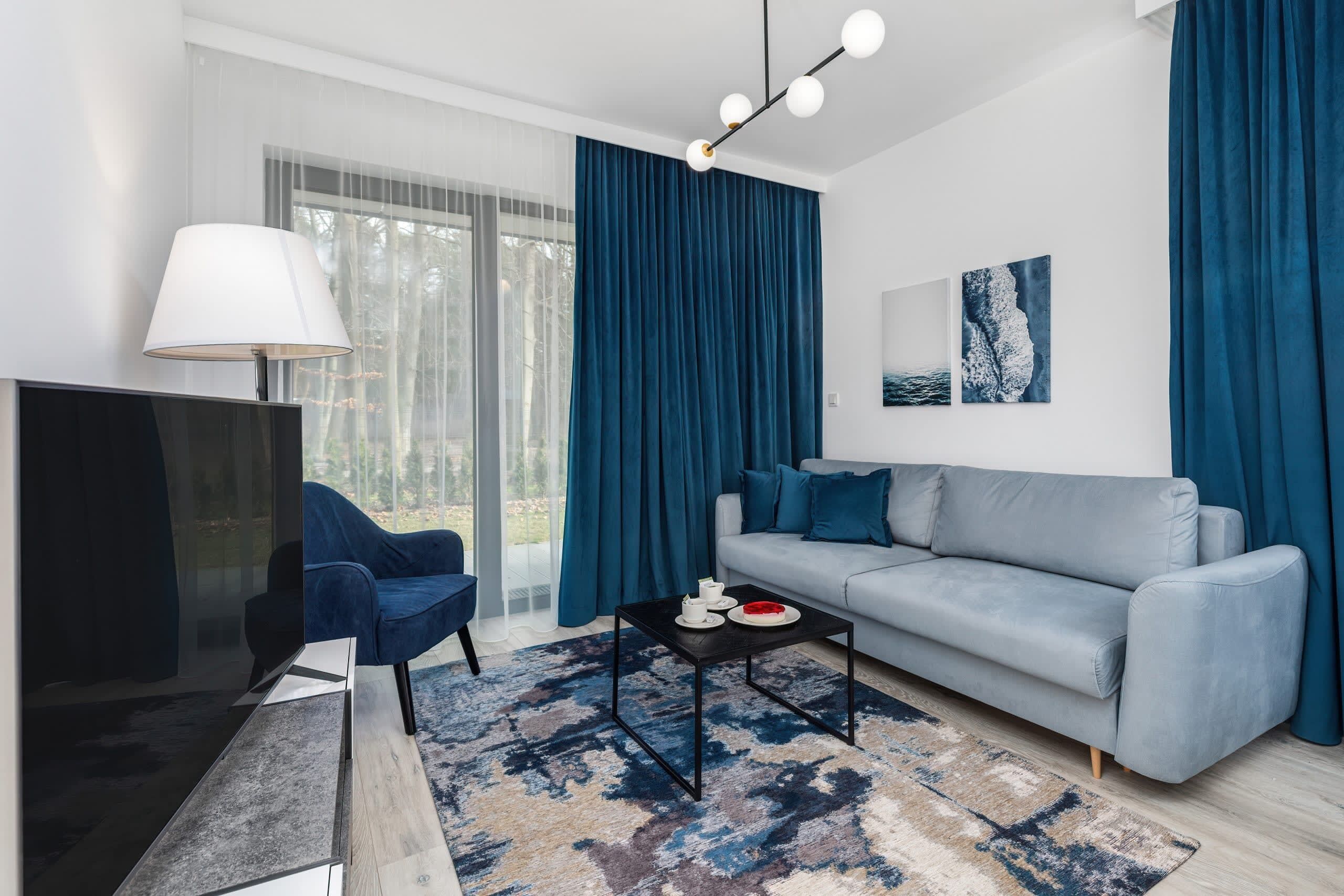 Ein modernes Wohnzimmer mit einem grauen Sofa, einem blauen Sessel, einem schwarzen Couchtisch und einem Fernseher.