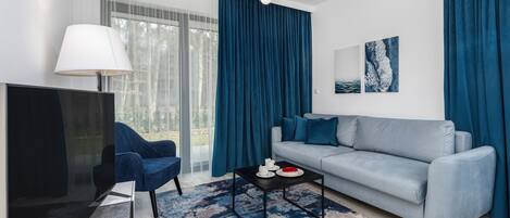 Ein modernes Wohnzimmer mit einem grauen Sofa, einem blauen Sessel, einem schwarzen Couchtisch und einem Fernseher.