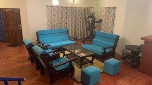 A living room with blue sofas, wooden chairs, a glass coffee table, and a decorative sculpture. - ONELOVEDALE Blusalz Homes (Ootacamund)