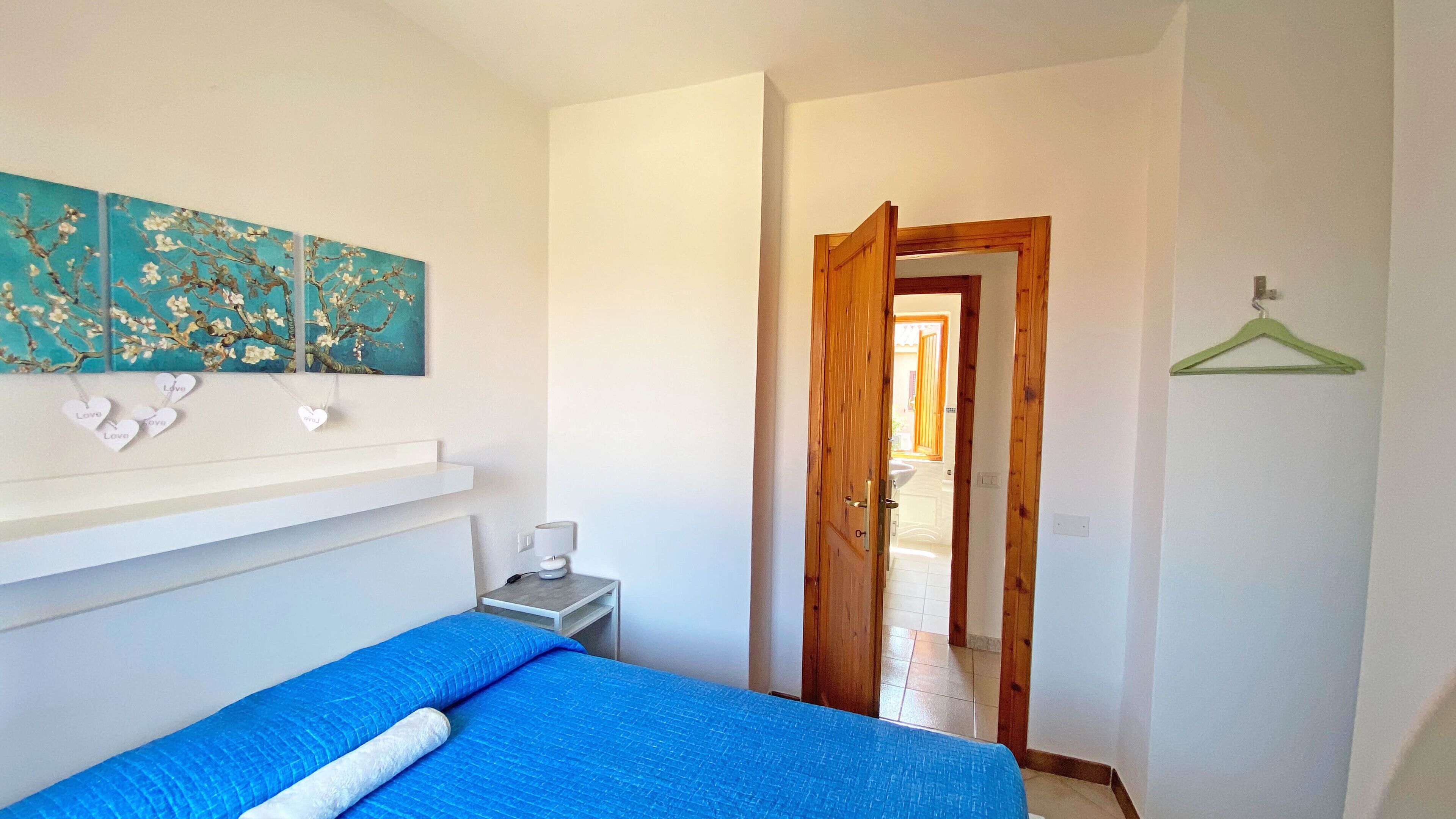 Une chambre à coucher comprenant un lit, une table de chevet, une étagère murale décorative et une porte donnant sur une autre pièce.