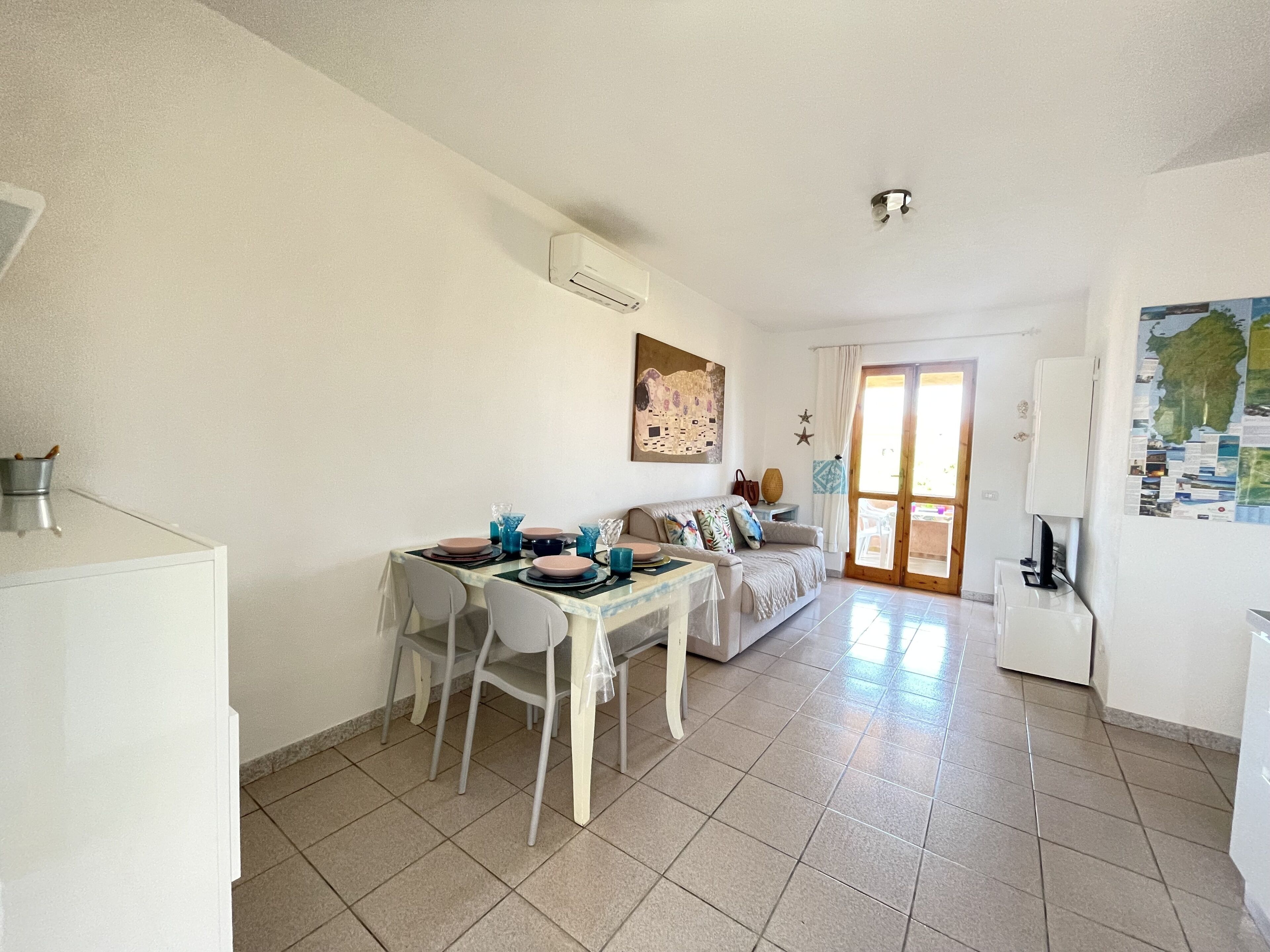 A dining area with a table set for four, a sofa, and a kitchen area with a refrigerator and a map on the wall.