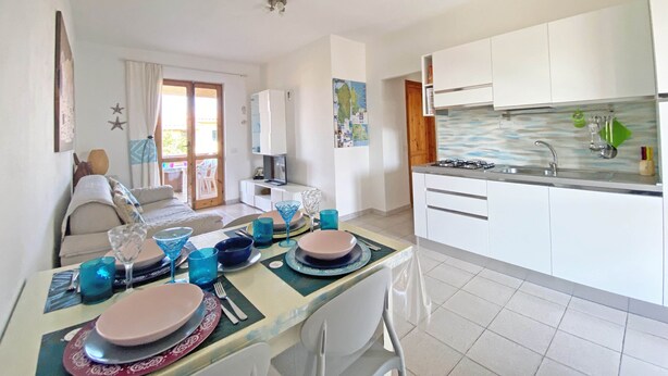 A modern kitchen with white cabinets, a gas stove, and a sink. There is a dining area with a table set for two, featuring blue glassware and plates.