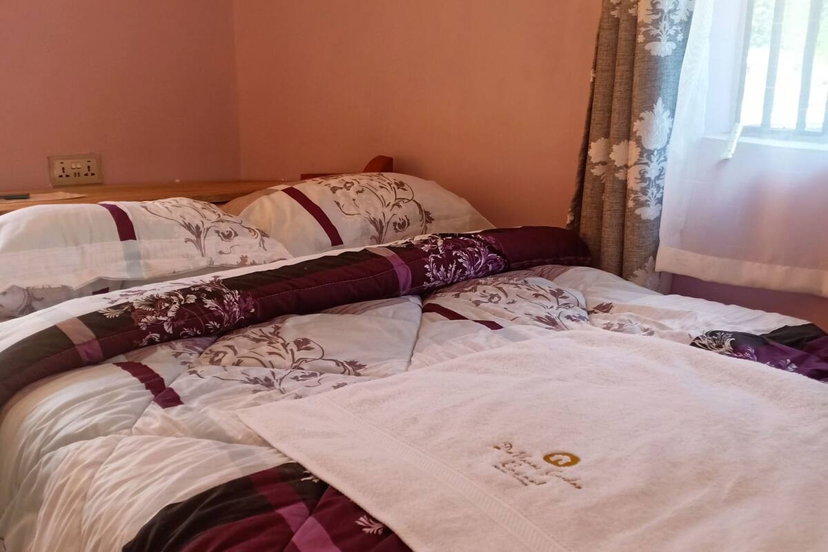 Una cama bien hecha con una colcha y almohadas estampadas con motivos florales, una manta blanca y una ventana con cortinas.