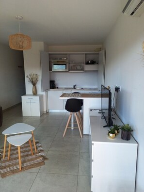 A modern kitchen with white cabinetry, a dining area with a small table and two chairs, and a hanging light fixture. - Studio de charme, Sea view, Port de Porto Vecchio, Swimming pool Terrace Parking WIFI (Porto-Vecchio)