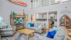A spacious living area with a large TV, multiple sofas, a coffee table, and a kitchen in the background. - Aqua Dreams | Pool • Game Room • Pets • Boat Park! (Port Aransas)