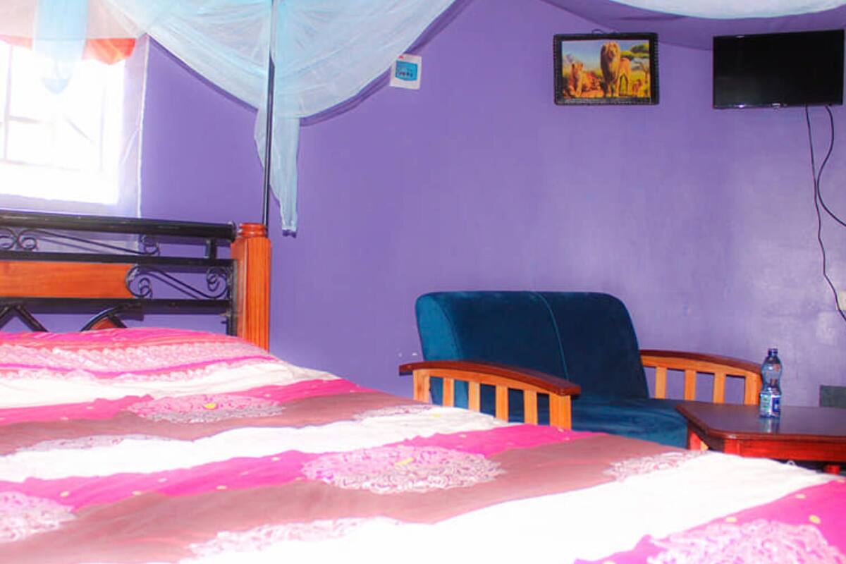 Une chambre à coucher avec un lit, une chaise, une table, un téléviseur et une fenêtre munie d’une moustiquaire.