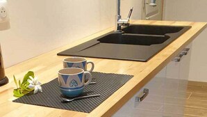 A kitchen with a wooden countertop, a black sink, and a built-in drawer unit with a glass door. - Moana Breeze Eco Lodge (Rangiroa)