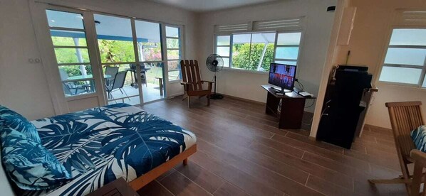 Une pièce spacieuse comprenant un lit, un bureau, une chaise, un ventilateur et un téléviseur.