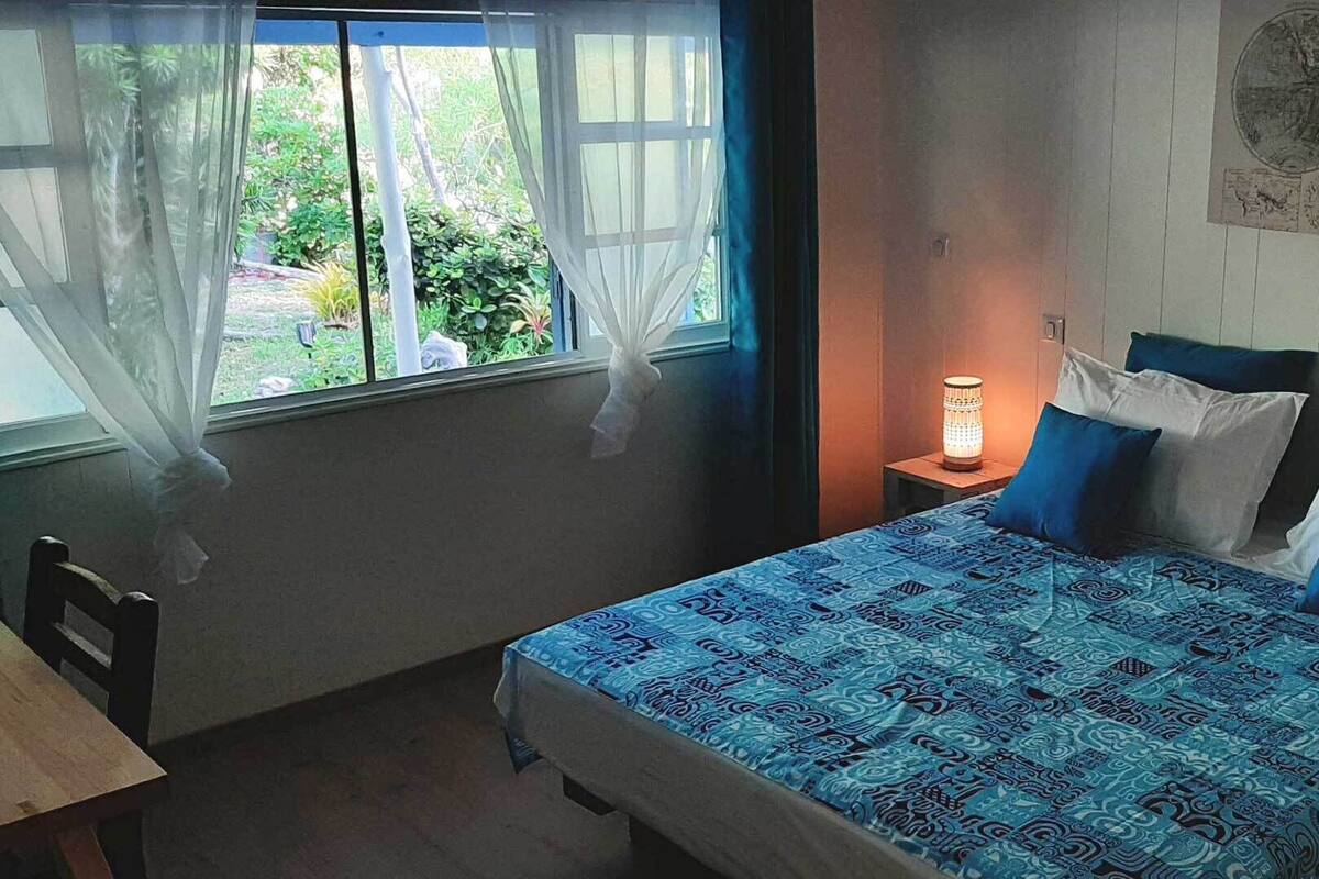 A bedroom with a bed, a nightstand, a lamp, a chair, and a window with curtains.