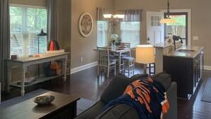 A spacious living room with a dark-colored sofa, a dining area with a table and chairs, a kitchen with a sink and countertop, and a ceiling fan.
