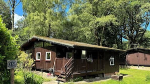 En rustik hytte med en træterrasse, en lille veranda og en sti til indgangen.