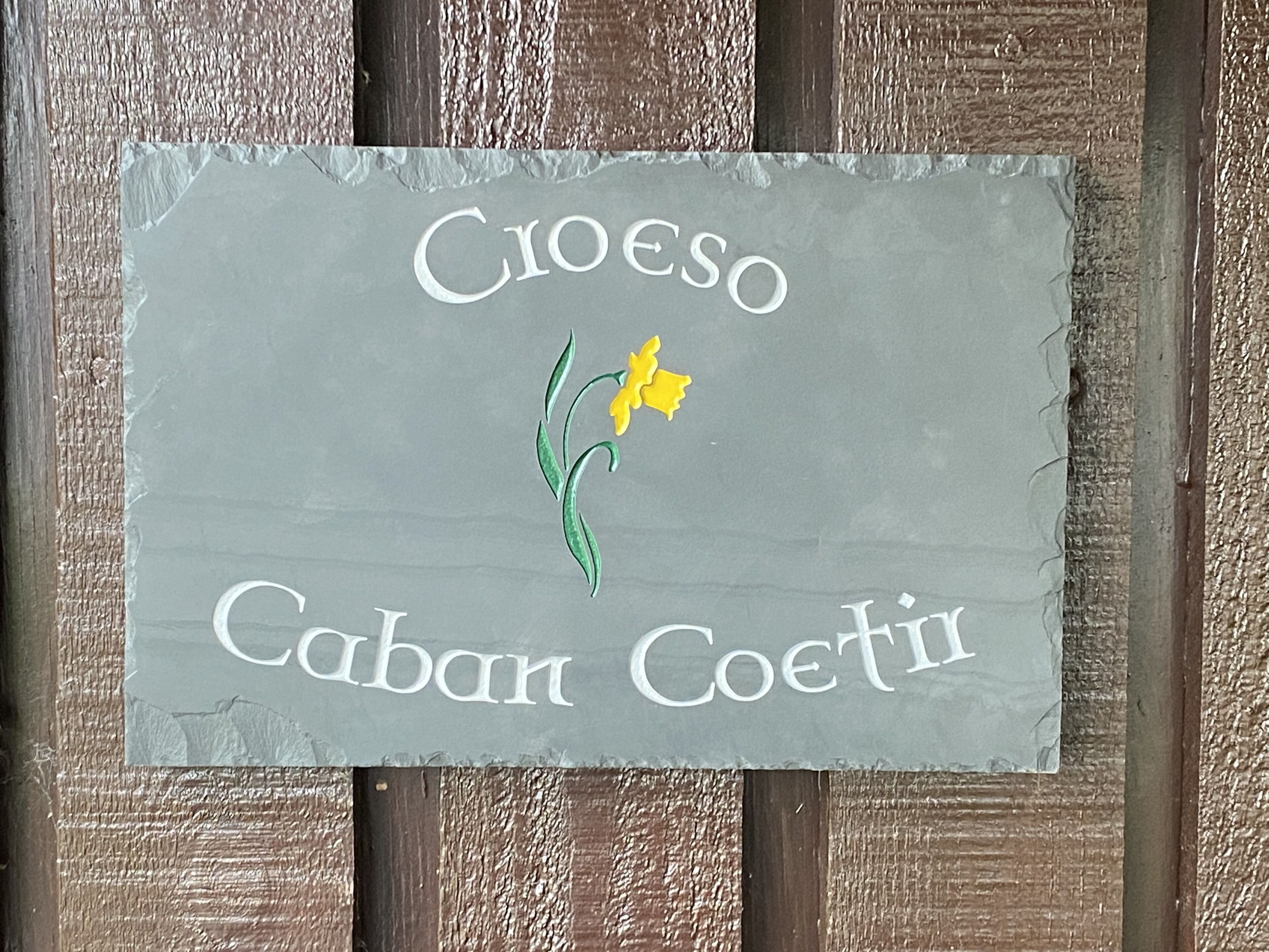 A slate sign with the text "Cioeso Caban Coetil" and a yellow flower illustration.
