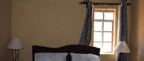 A bedroom with a bed, two nightstands, a window with curtains, and a wall-mounted light fixture.