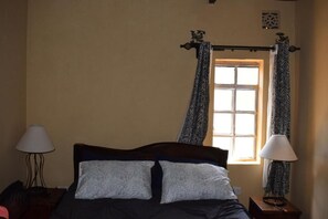 Quarto com uma cama, duas mesas de cabeceira, uma janela com cortinas e um candeeiro fixo na parede.