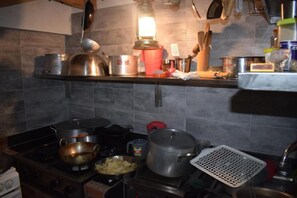 Uma cozinha com fogão a gás, panelas, frigideiras e luminária pendente.