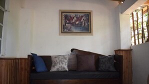 A wooden sofa with multiple cushions in a room with a white wall and a framed painting above it. - Kileefarm Cottages (Nguluni)
