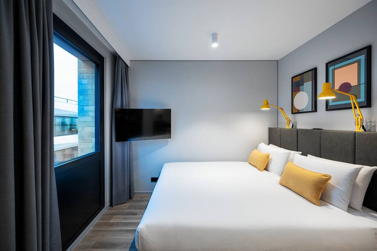 A modern hotel room with a large bed, a flat-screen TV, and two bedside lamps.