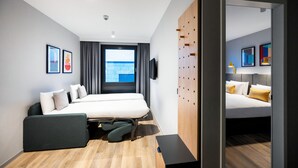 Quarto de hotel moderno com uma cama grande, uma escrivaninha, uma cadeira, uma televisão e uma janela com cortinas.