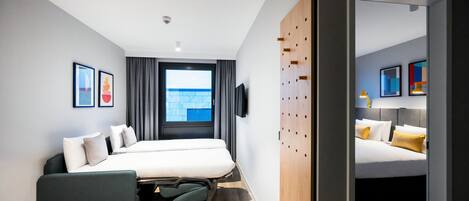 A modern hotel room with a large bed, a desk, a chair, a TV, and a window with curtains.