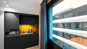 Cozinha moderna com armários pretos, bancada de madeira e vista para um edifício por uma grande janela.