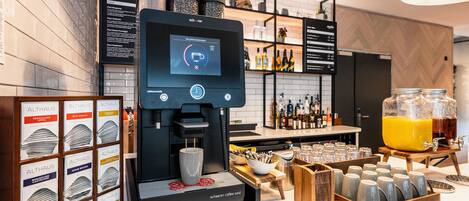 Ein modernes Café mit einer digitalen Kaffeemaschine, einer Auswahl an Kaffeekapseln und einem großen Krug Orangensaft.