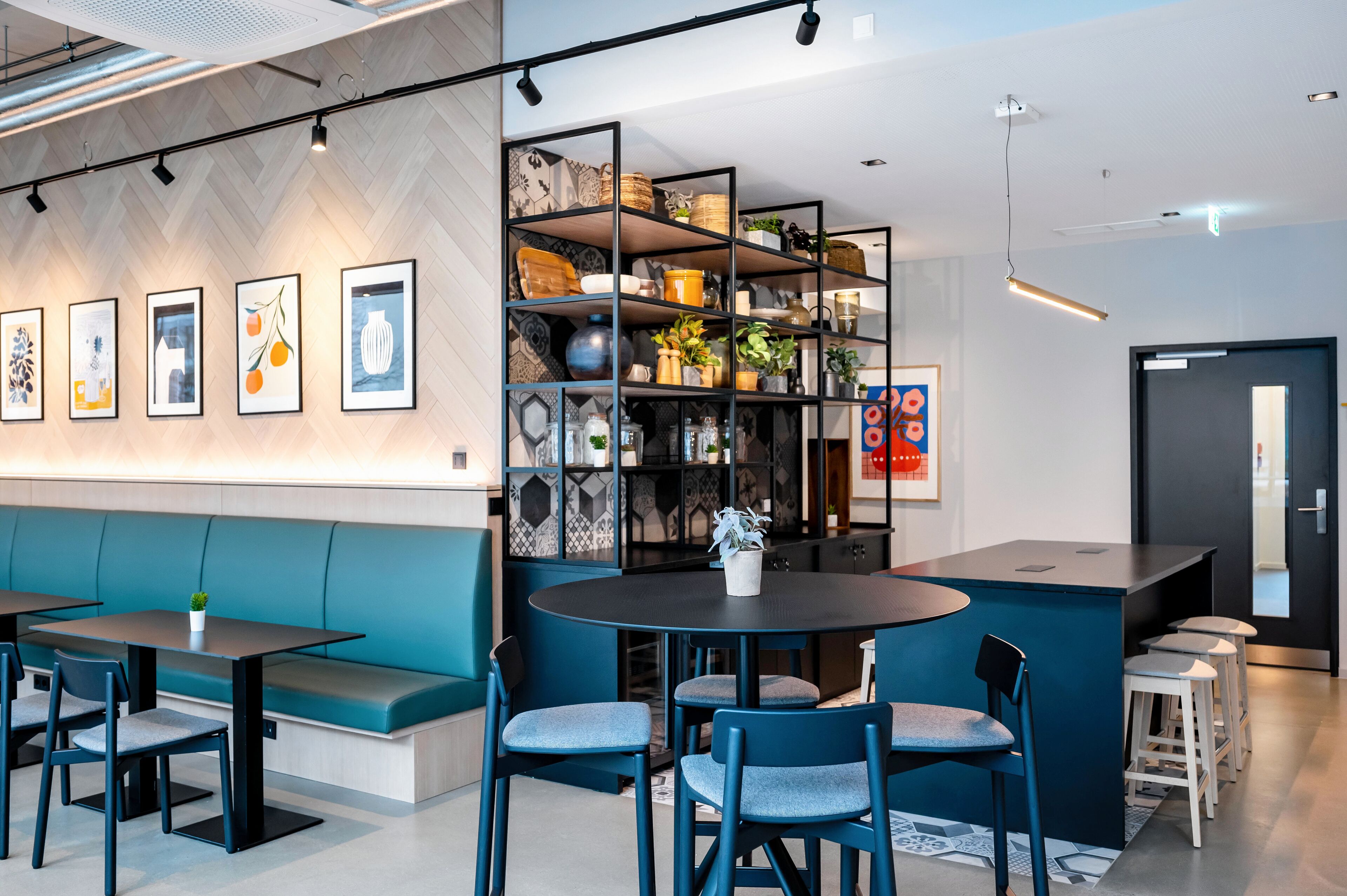 Ein modernes Café mit einer blauen Sitzgruppe, einem runden Tisch und einem Bücherregal mit unterschiedlichen Gegenständen.
