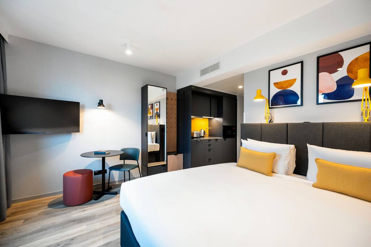 A modern hotel room with a large bed, a desk, and a seating area.