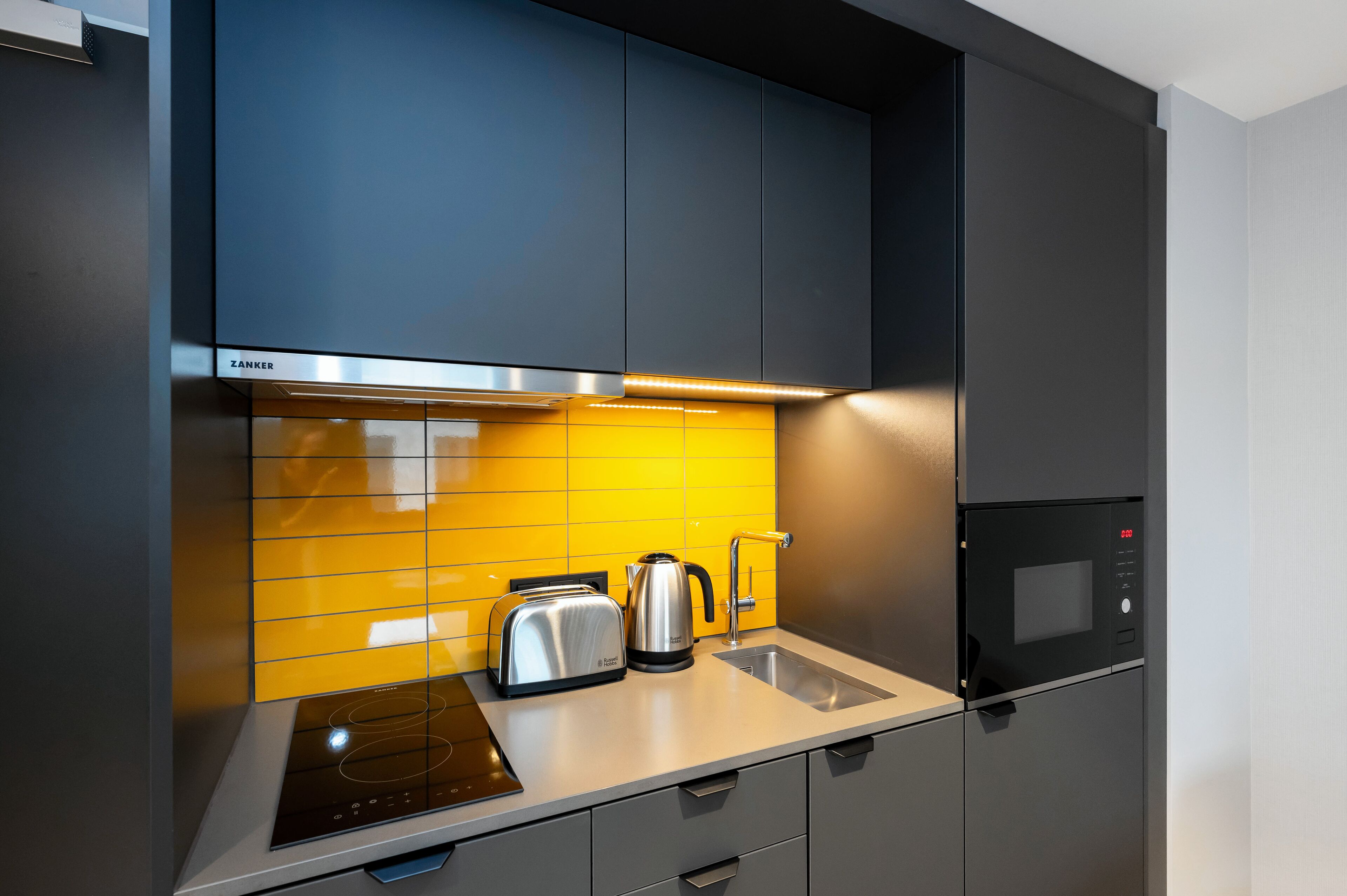 Een moderne keuken met een Zanker afzuigkap, een inbouwmagnetron en een waterkoker op het aanrecht.