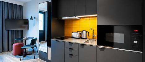 Una cocina moderna con microondas, tostadora y hervidor, un pequeño comedor con mesa y sillas, y un espejo grande.
