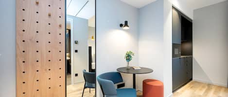 Una habitación moderna con un separador de madera, dos sillas, una mesita con una planta y un reposapiés rojo.