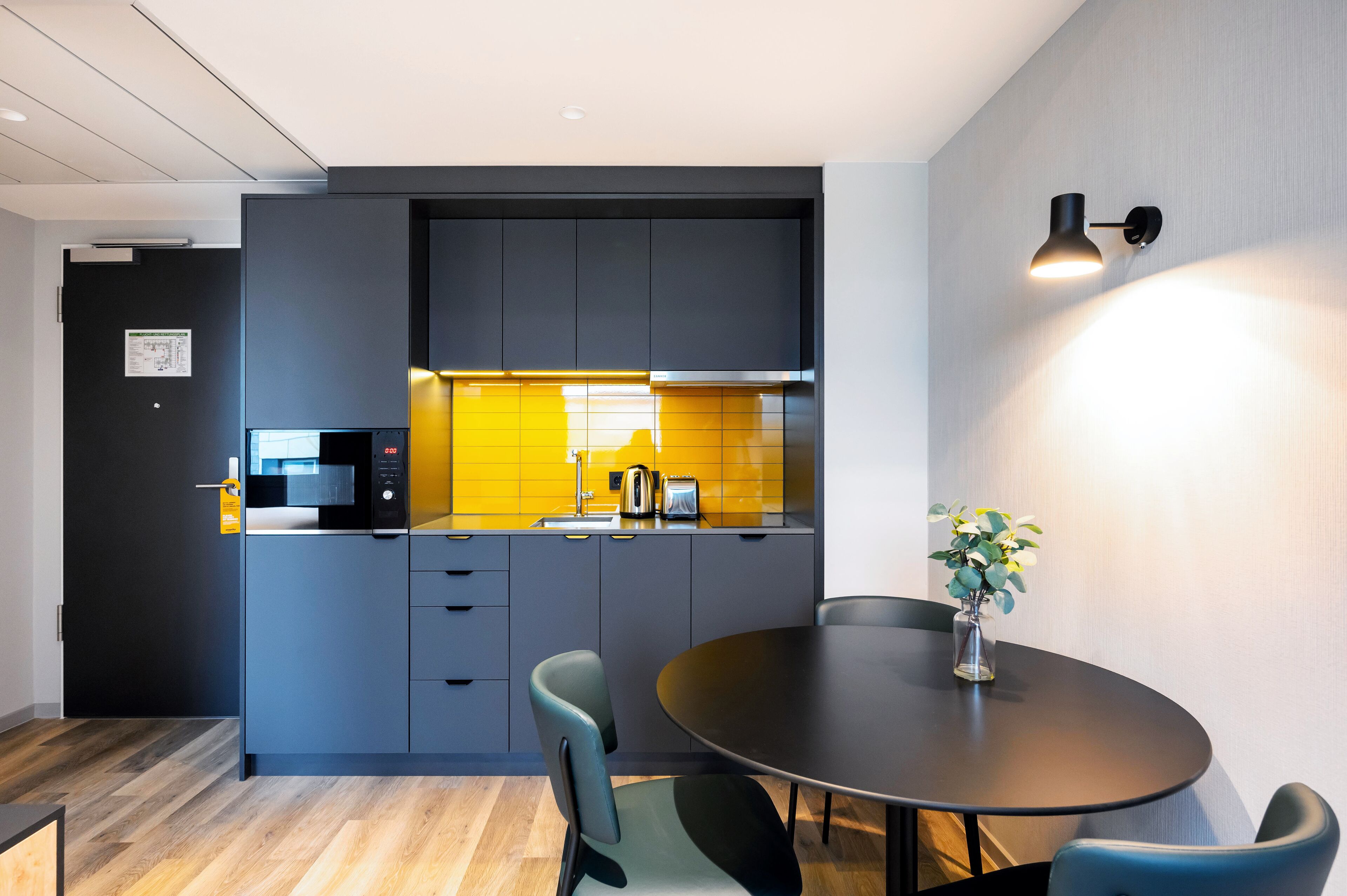 Una cocina moderna con armarios oscuros, un salpicadero amarillo y una zona de comedor con una mesa redonda y sillas.