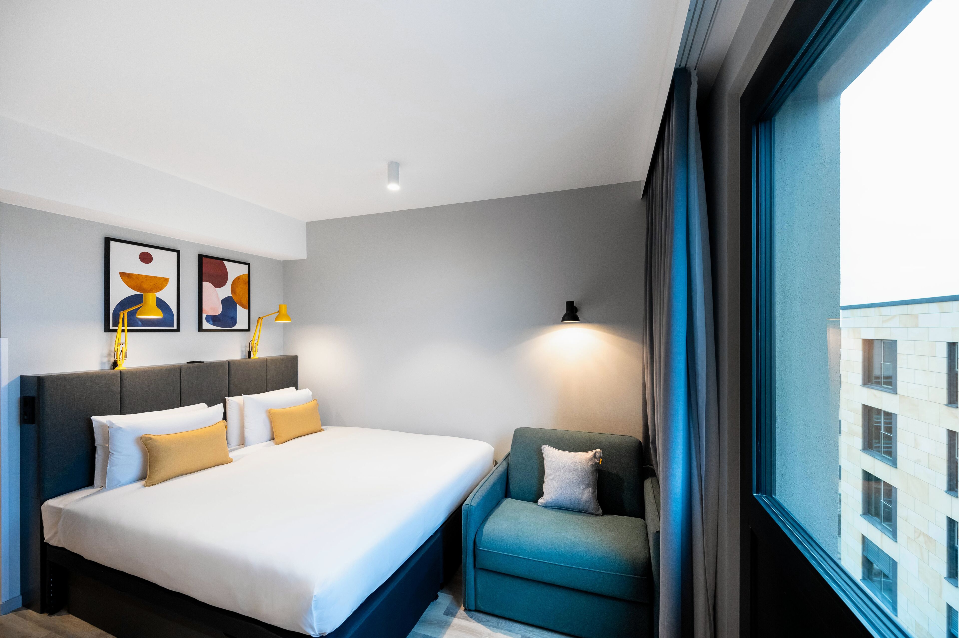 Habitación de hotel con cama, una silla, ventana y obras de arte en la pared.