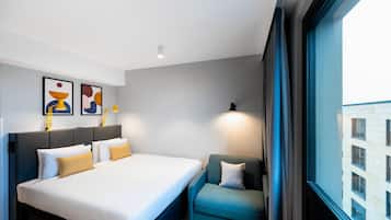 Habitación de hotel con cama, una silla, ventana y obras de arte en la pared.