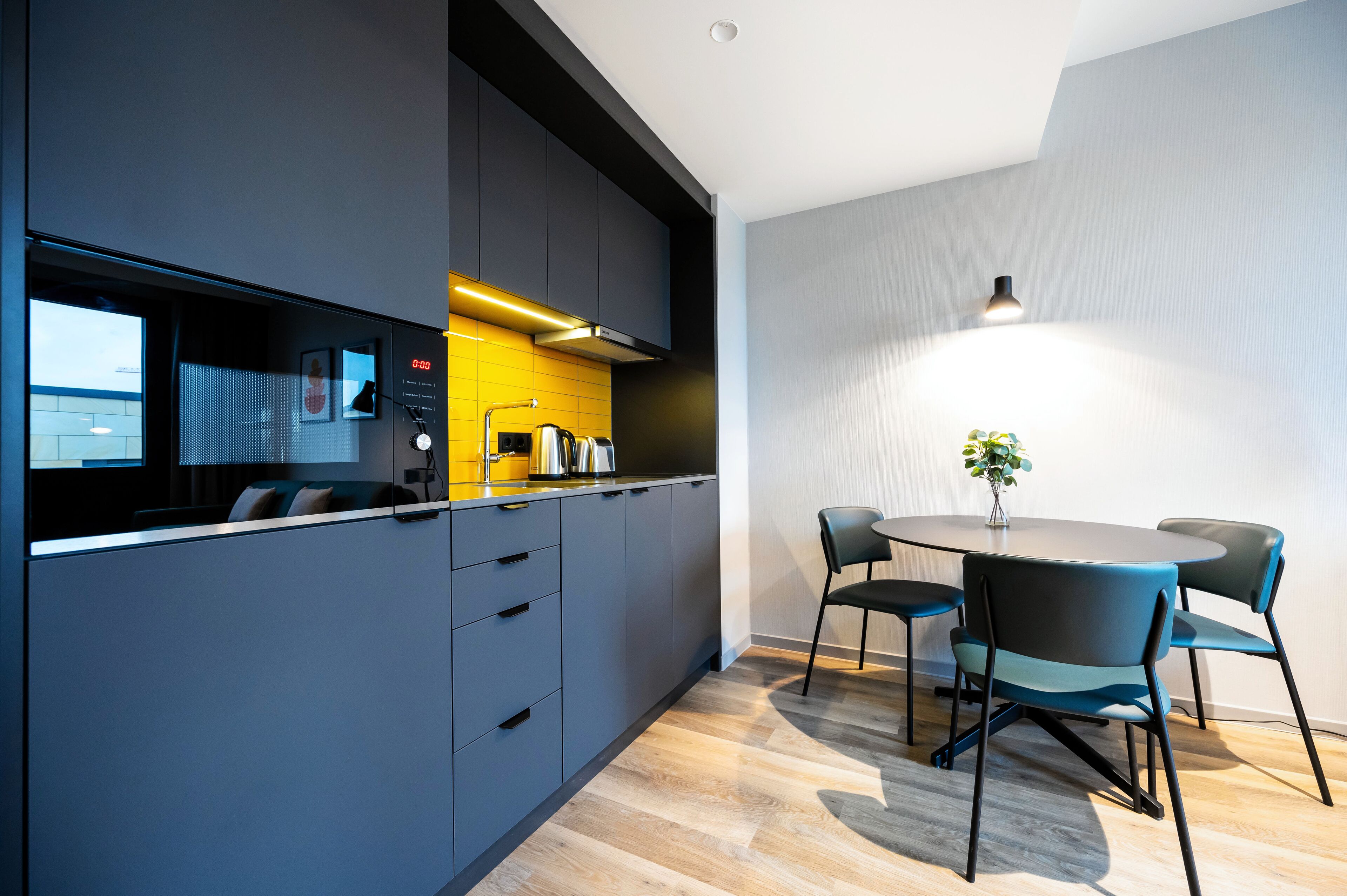 A modern kitchen with dark cabinetry, a yellow backsplash, and a round dining table with four chairs.