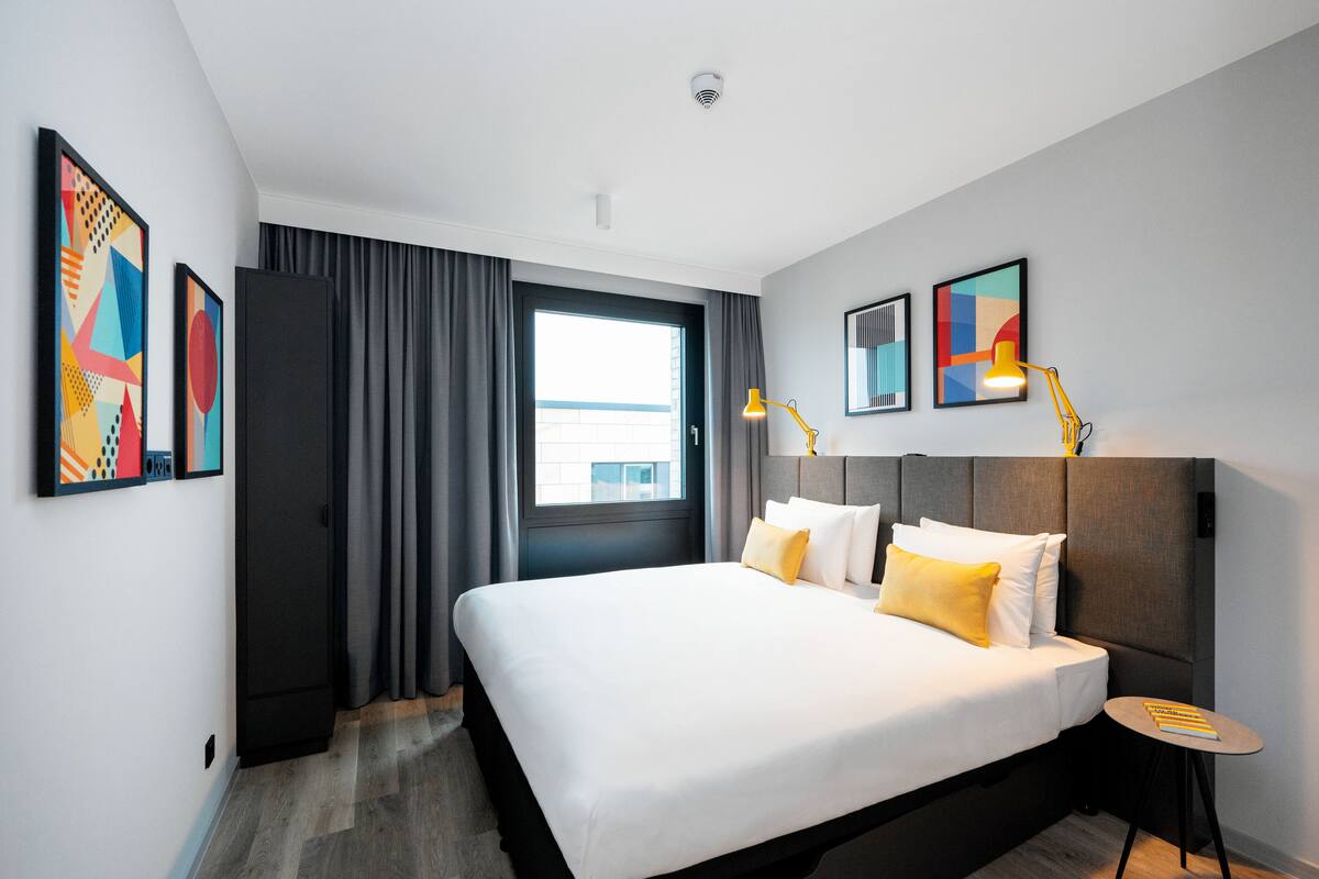 A modern hotel room with a large bed, a small side table, and artwork on the walls.