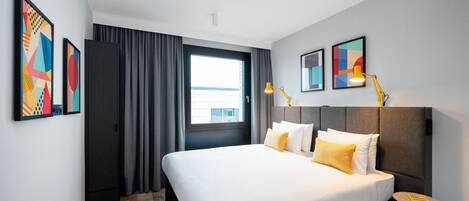 A modern hotel room with a large bed, a small side table, and artwork on the walls.