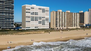 Un hotel frente a la playa con varias construcciones, una playa de arena y olas oceánicas.