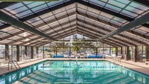 Una piscina interior con techo de vidrio, rodeada de sillones de descanso y vistas al exterior.