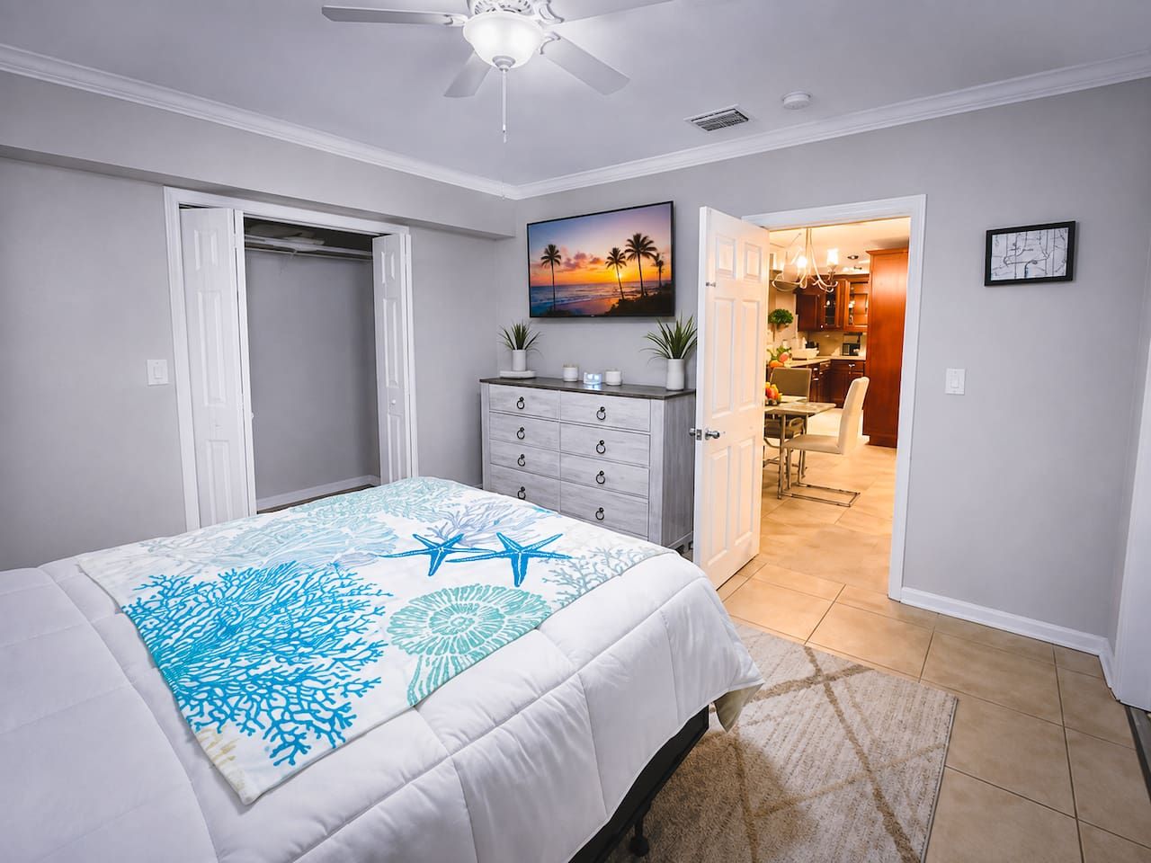 A bedroom with a bed, a dresser, a television, and a view into the dining area.