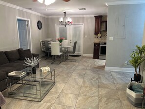 A living room with a glass coffee table, a sofa, and a dining area with chairs and a table.