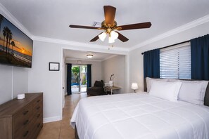 A hotel room with a bed, a desk, a chair, a ceiling fan, and a painting on the wall.