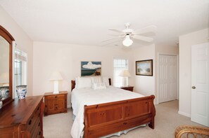 A bedroom with a wooden bed, two bedside tables with lamps, a ceiling fan, a large mirror, and a door.