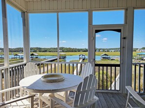 A covered outdoor area with a table and chairs, overlooking a water body and distant houses.