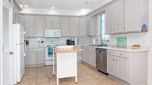 A modern kitchen with white cabinetry, a microwave, a stove, a dishwasher, and a wooden island. - Creek Front Beach House, 3 Screened Porches, Private Dock, Easy Walk to Beach (Pawleys Island)